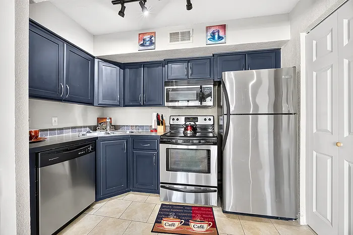 Chic kitchen with sleek stainless steel appliances, dark blue cabinets, and modern tile flooring.