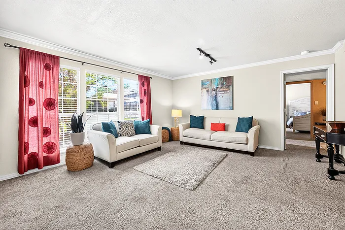 Bright and inviting living room featuring plush carpets, elegant white sofas with colorful cushions, modern artwork, and large windows with vibrant red curtains.