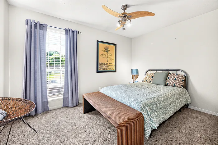Charming bedroom with natural light, featuring cozy bedding, stylish wooden bench, and modern ceiling fan for a serene atmosphere.