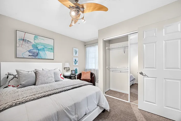 Inviting bedroom with stylish decor, featuring a comfortable bed, artistic wall art, ceiling fan, and a spacious closet.