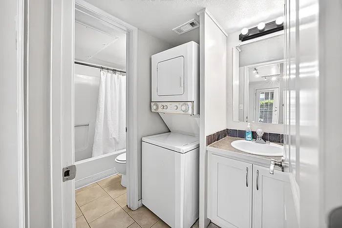 Bright and functional bathroom with an in-unit washer and dryer, elegant vanity, and modern lighting fixtures.
