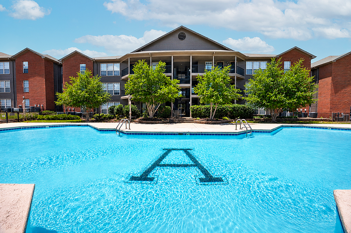Inviting apartment complex with a sparkling blue pool, lush greenery, and red brick buildings showcasing luxurious living.