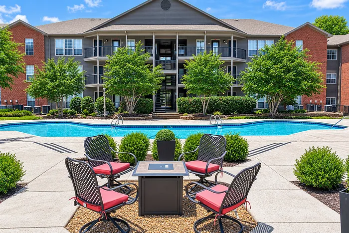 Beautiful apartment complex with a sparkling pool, lush greenery, and stylish outdoor seating, perfect for relaxation and leisure.