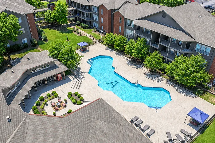 Aerial view of a beautifully landscaped apartment complex featuring a sparkling pool with ample lounging areas and lush greenery.