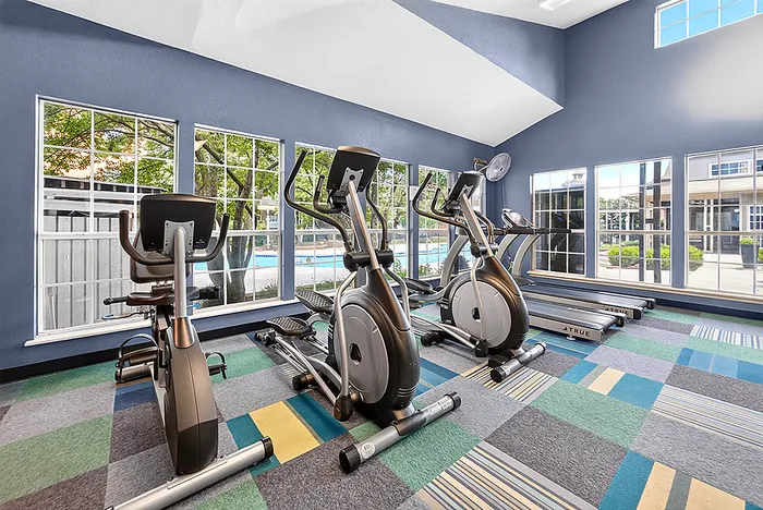 Bright fitness center with modern elliptical machines and large windows overlooking a pool area.