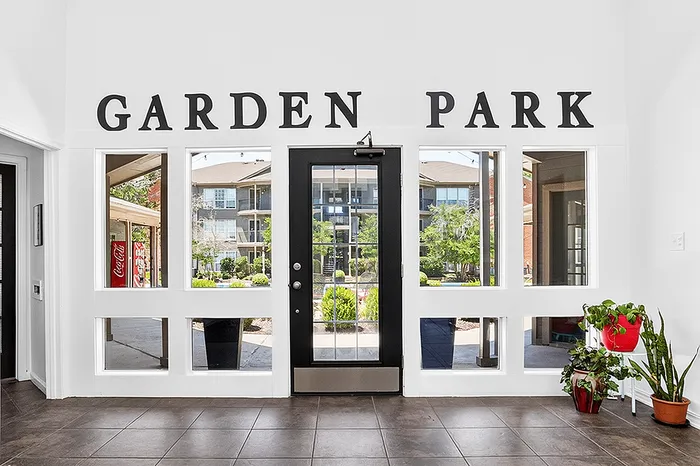 Inviting entrance to Garden Park with lush garden views, modern glass door, and elegant indoor plants.