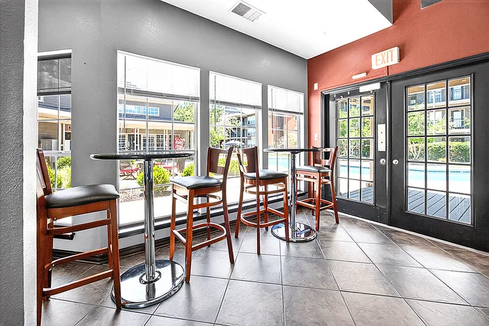 Inviting lounge area with sleek high-top tables and chairs, large windows offering a view of the vibrant courtyard and pool outside.