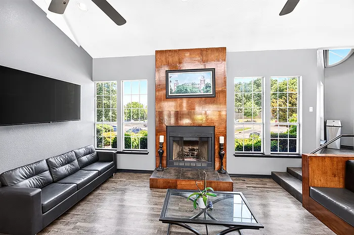 Modern living room with sleek leather couch, elegant fireplace, and large sunlit windows offering scenic views.