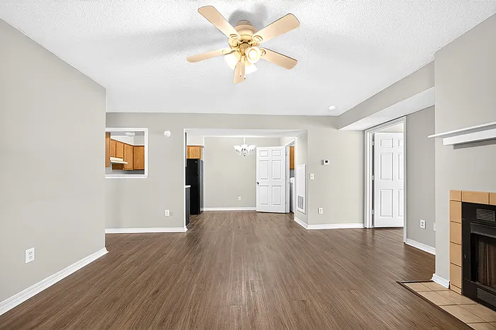 Inviting open-concept living area with elegant ceiling fan, gleaming wood floors, and cozy fireplace, leading to a modern kitchen.