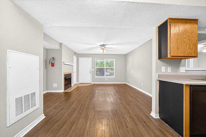 Bright and spacious open-plan room with elegant hardwood flooring, featuring a cozy fireplace and large window for ample natural light.