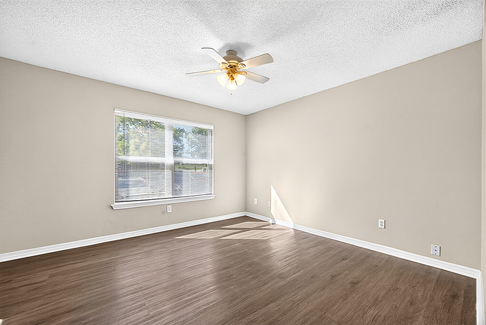 Bright and spacious room with elegant wood flooring, large window for natural light, and sleek ceiling fan, ideal for a cozy living space.