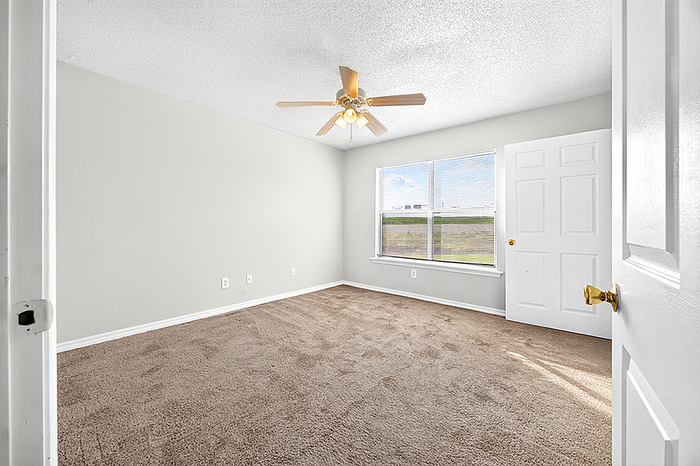 Bright and airy bedroom with plush carpet, modern ceiling fan, and large window offering scenic views.