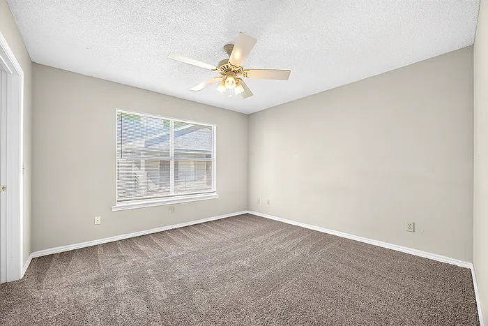 Bright and spacious room with plush carpet, neutral walls, and a ceiling fan, ideal for a cozy bedroom setup.