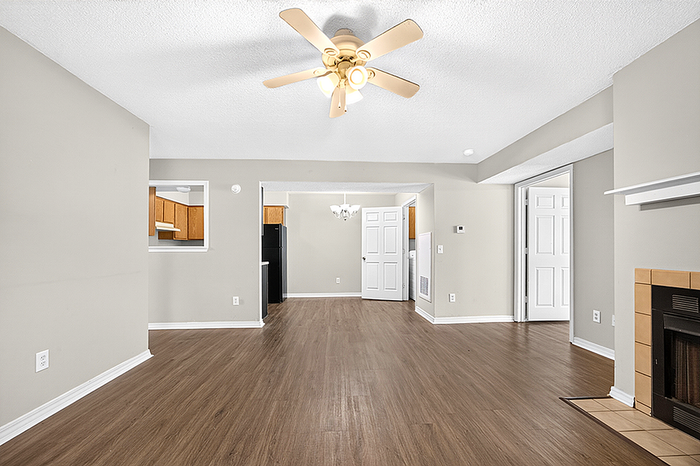 Elegant open-concept living area with modern ceiling fan, hardwood floors, and a cozy fireplace, seamlessly leading to a bright kitchen and dining space.
