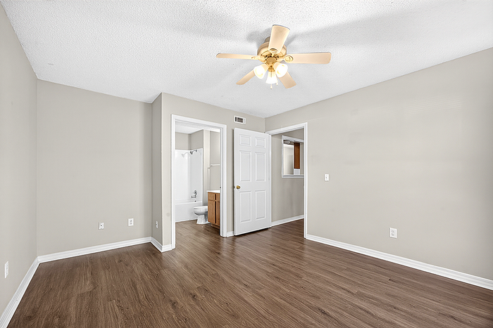 Bright and airy bedroom with elegant hardwood flooring, ceiling fan, and an en-suite bathroom, offering a modern and inviting living space.