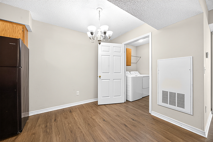 Charming laundry area with modern washer and dryer set, elegant chandelier, and sleek hardwood flooring.