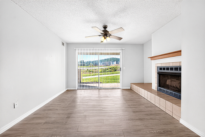 Bright and spacious living room with sleek wood flooring, elegant fireplace, and large glass doors opening to a scenic balcony view.