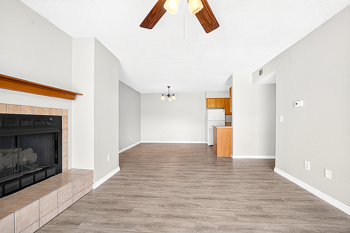 Inviting open-concept living area with a cozy fireplace, elegant wood flooring, and a modern kitchen tucked in the corner.
