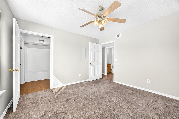 Bright and airy bedroom with plush carpet, ceiling fan, and ample natural light, offering a peaceful and inviting atmosphere.