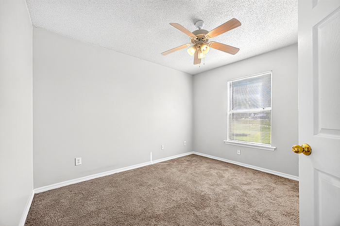 Bright and airy bedroom with plush carpet, large window, and elegant ceiling fan, perfect for a cozy retreat.