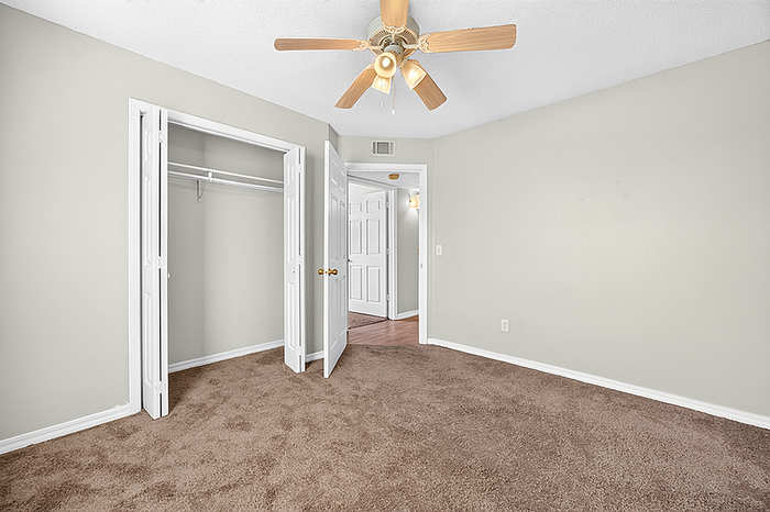 Inviting bedroom with cozy carpet, spacious closet, and elegant ceiling fan, offering a comfortable living atmosphere.