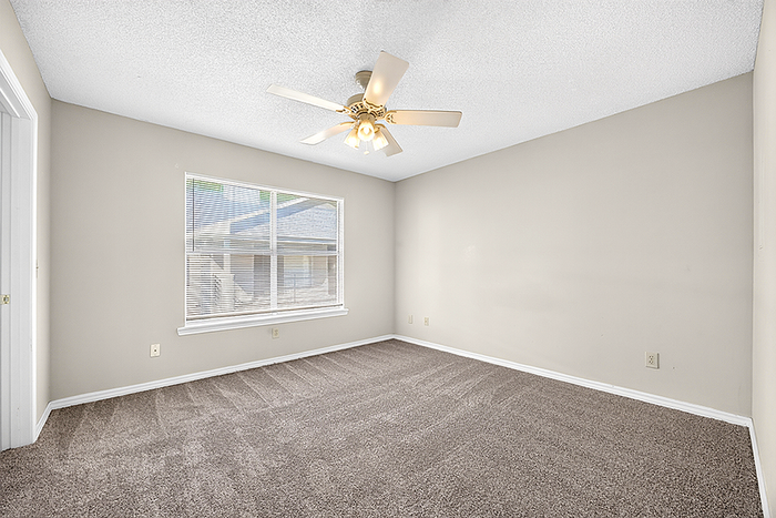 Bright and inviting bedroom with soft carpeting, large window, and ceiling fan, perfect for relaxation.