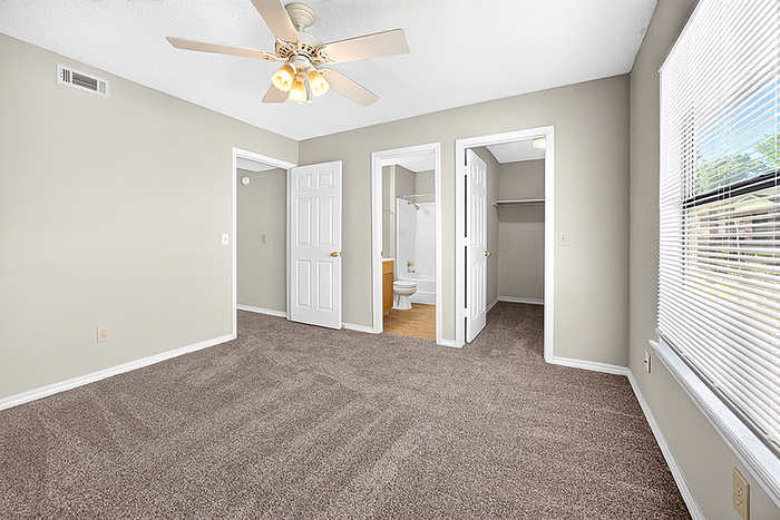 Bright, airy bedroom with plush carpet and ceiling fan, featuring adjacent bathroom and walk-in closet for optimal convenience.