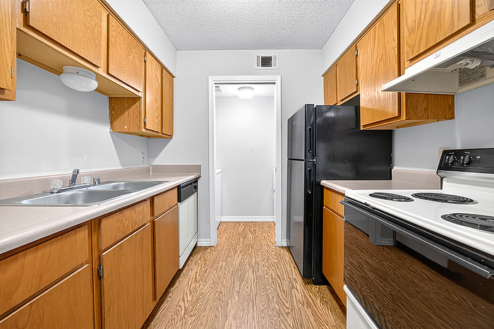 Modern galley kitchen with warm wooden cabinets, sleek black appliances, and elegant countertops.