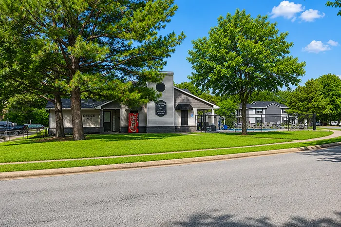 Inviting apartment community with lush green surroundings, featuring a stylish office building and modern amenities under a bright blue sky.