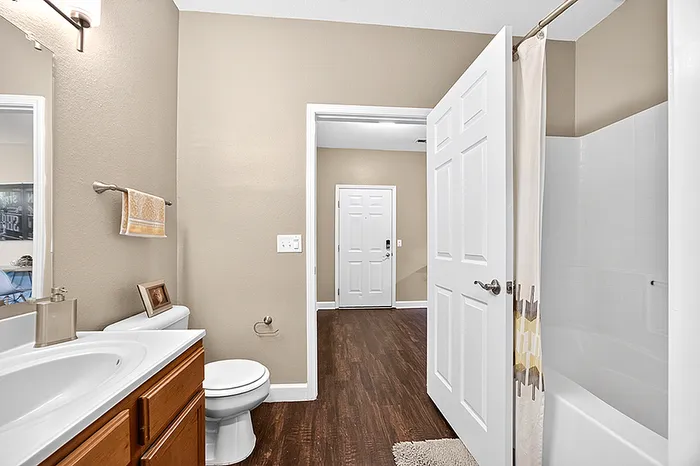 Inviting bathroom with modern fixtures, elegant vanity, and warm wooden flooring extending to a welcoming entrance.