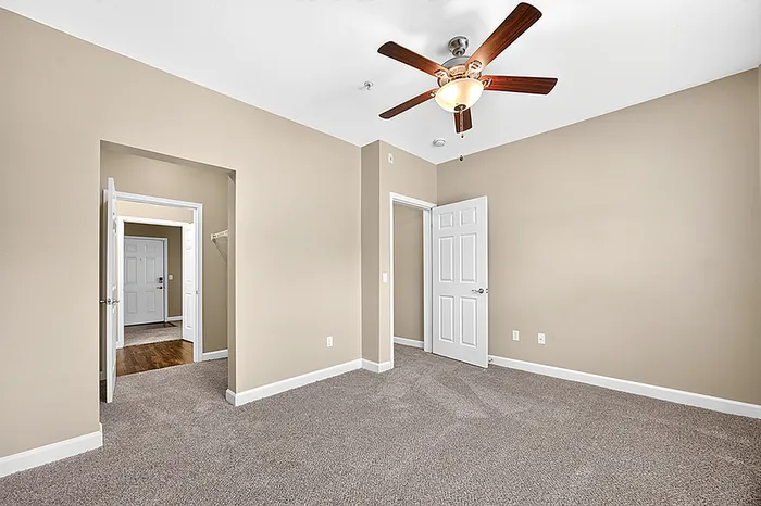 Bright and inviting bedroom with plush carpet and a sleek ceiling fan, showcasing a walk-in closet and modern doors.