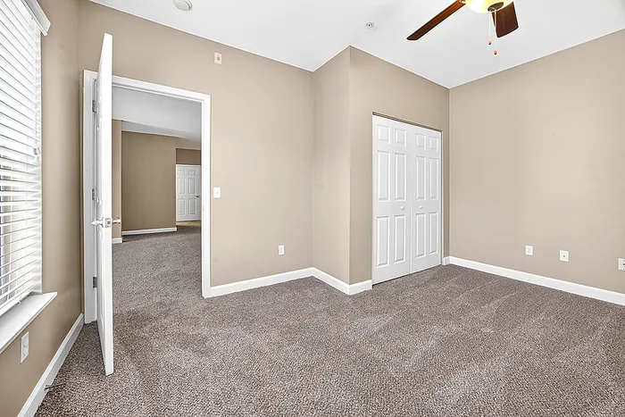 Bright, spacious bedroom with cozy carpeting and modern ceiling fan, showcasing ample natural light and convenient double-door closet access.