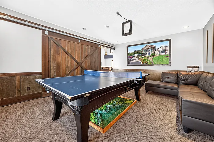 Modern recreation room featuring a sleek ping pong table, stylish leather couch, and rustic barn door design.