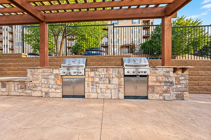 Elegant outdoor grilling area with modern stainless steel barbecue grills, surrounded by stylish stonework and wooden pergola.