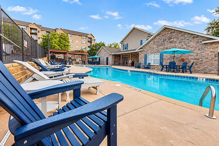Inviting outdoor pool area with stylish blue lounges, surrounded by modern apartments and lush greenery.