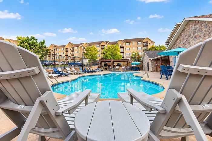 Inviting community swimming pool area with comfortable lounge chairs and scenic apartment backdrop.