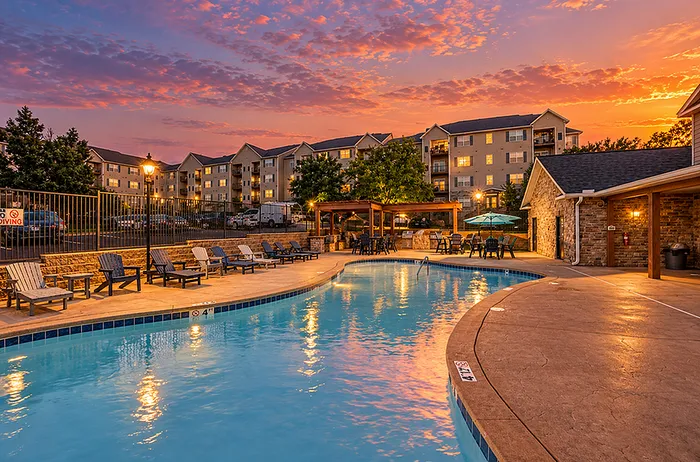 Charming apartment complex at sunset featuring a pristine swimming pool, cozy seating areas, and inviting pergolas.