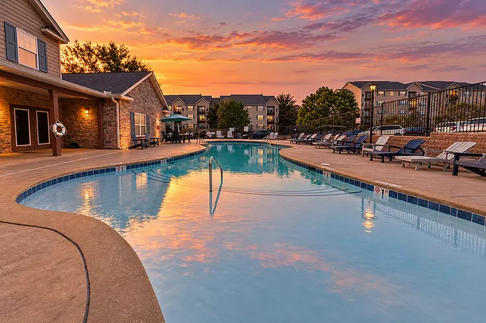 Inviting outdoor pool area with serene sunset reflections, surrounded by cozy lounge chairs and scenic apartment views.