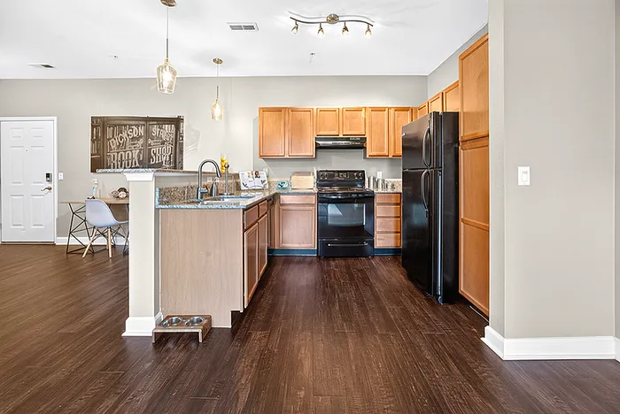 Bright, modern kitchen with sleek cabinetry, granite countertops, and stylish lighting, opening into a spacious hardwood-floored dining area.