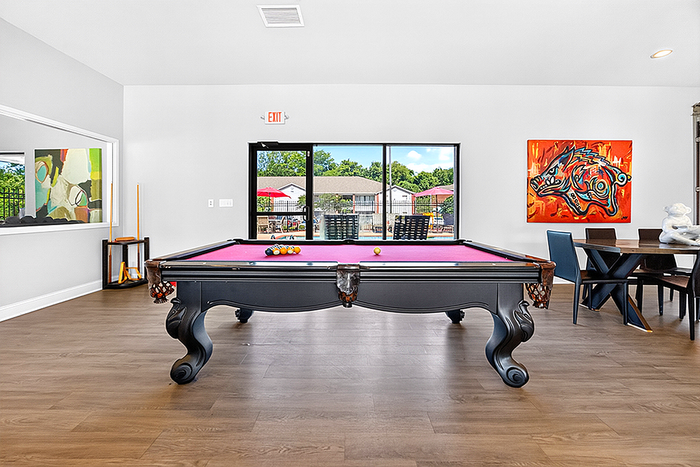 Vibrant recreation room featuring a pool table with a stylish red felt top, modern artwork, and outdoor views through large windows.