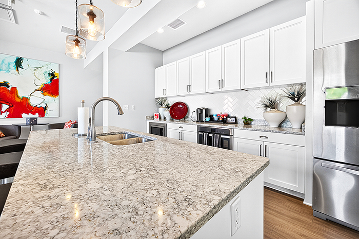 Modern kitchen with elegant granite island, sleek white cabinets, and stylish lighting, perfect for entertaining.