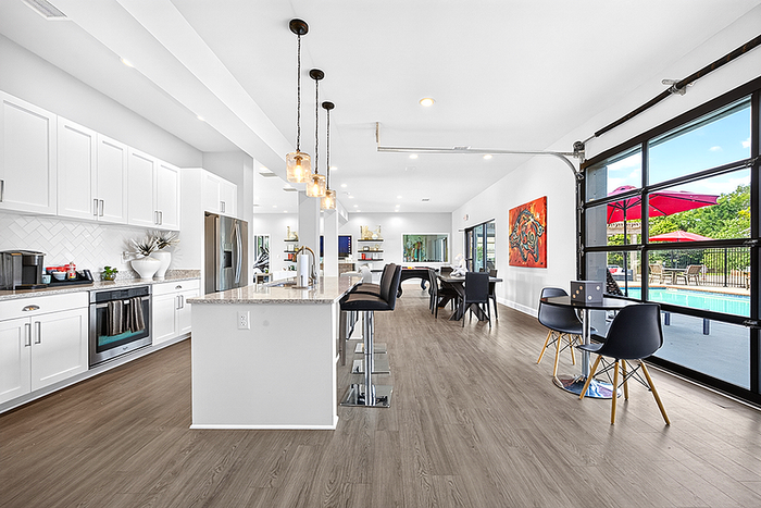 Elegant open-concept kitchen and dining area with modern lighting, sleek cabinetry, and view of a poolside patio through expansive glass doors.