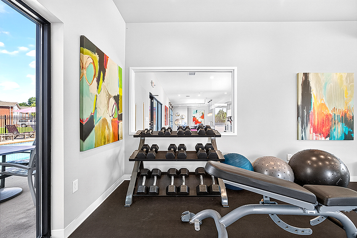 Modern fitness center with an array of dumbbells, vibrant abstract art, and a glimpse of an inviting poolside area.