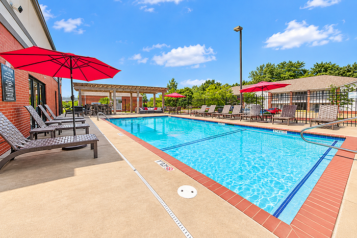 Inviting outdoor swimming pool with stylish lounge chairs and vibrant red umbrellas under a clear blue sky.