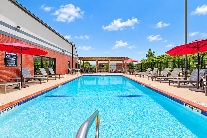 Vibrant outdoor swimming pool with red umbrellas and comfortable lounge chairs under a bright blue sky, perfect for relaxation.
