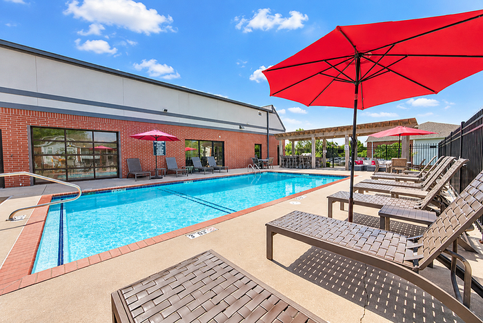 Inviting outdoor pool area with red umbrellas and lounge chairs, perfect for relaxation under a bright blue sky.