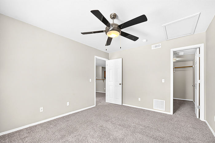 Bright, spacious bedroom with plush carpeting, modern ceiling fan, and walk-in closet for luxurious living.