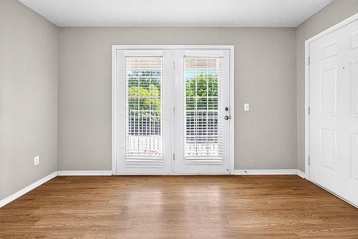 Bright room featuring elegant French doors with white blinds, leading to a scenic outdoor view, complemented by pristine hardwood floors.