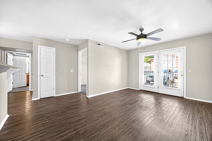 Bright and spacious living room with elegant wood flooring, ceiling fan, and double glass doors leading to a charming balcony.