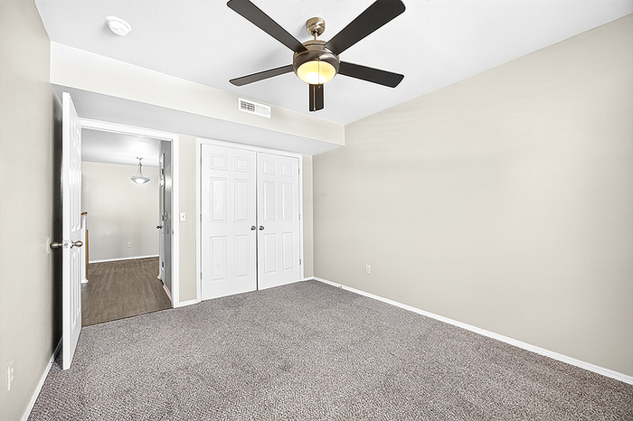 Spacious bedroom with modern ceiling fan, plush carpeting, and ample natural light.